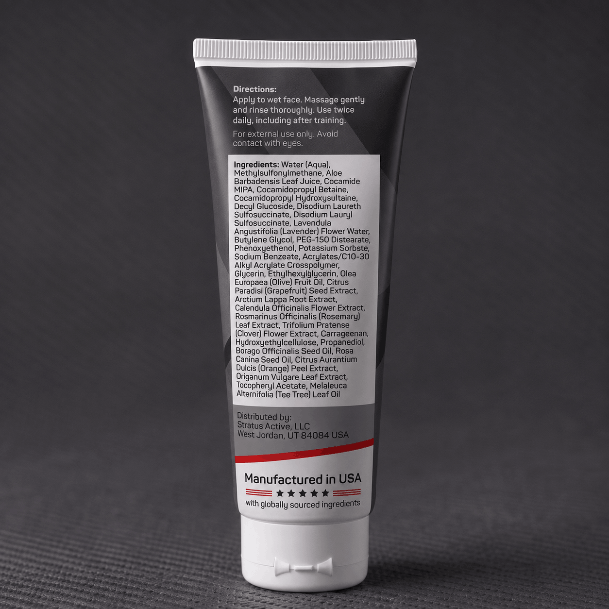 A dark squeeze tube of Stratus Performance Facial Cleanser, part of a post workout skincare routine, standing upright on a dark gray textured surface. The back view including ingredients is shown.