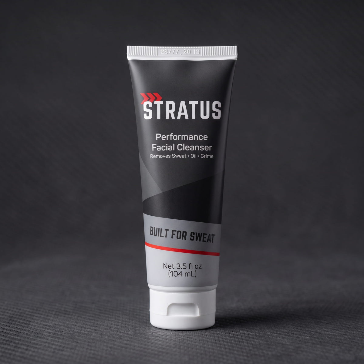 A tube of Stratus Performance Facial Cleanser, part of a post workout skincare routine, standing upright on a dark gray textured surface.