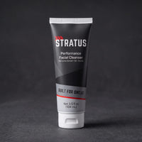 A tube of Stratus Performance Facial Cleanser, part of a post workout skincare routine, standing upright on a dark gray textured surface.