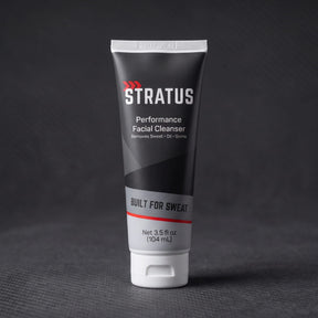 A tube of Stratus Performance Facial Cleanser, part of a post workout skincare routine, standing upright on a dark gray textured surface.