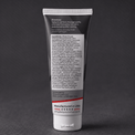 A dark squeeze tube of Stratus Performance Facial Cleanser, part of a post workout skincare routine, standing upright on a dark gray textured surface. The back view including ingredients is shown.