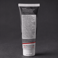 A dark squeeze tube of Stratus Performance Facial Cleanser, part of a post workout skincare routine, standing upright on a dark gray textured surface. The back view including ingredients is shown.