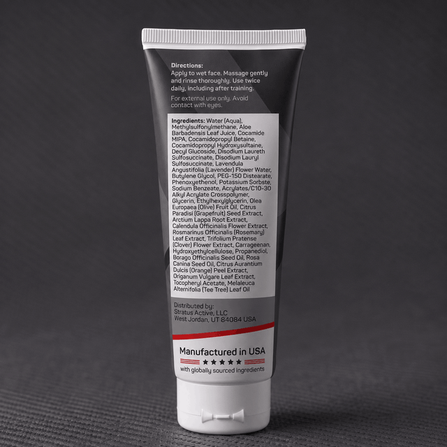 A dark squeeze tube of Stratus Performance Facial Cleanser, part of a post workout skincare routine, standing upright on a dark gray textured surface. The back view including ingredients is shown.