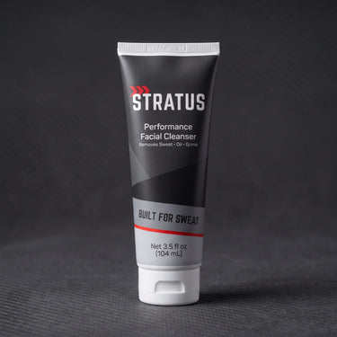 A tube of Stratus Performance Facial Cleanser, part of a post workout skincare routine, standing upright on a dark gray textured surface.