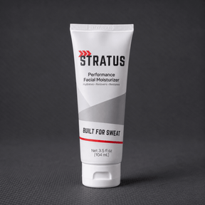 A white squeeze tube of Stratus Performance Facial Moisturizer, part of a post workout skincare routine, standing upright on a dark gray textured surface.
